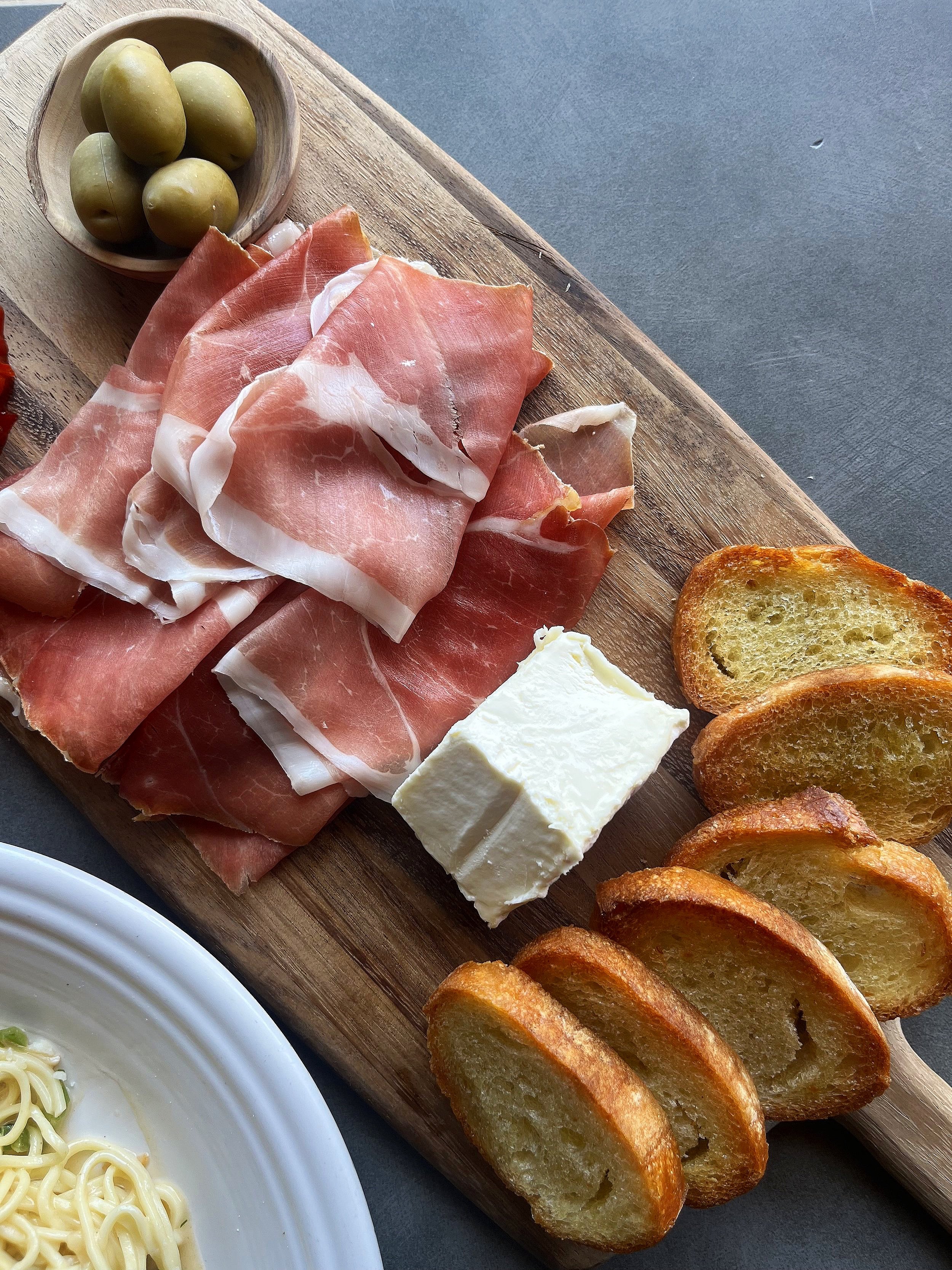 A charcuterie board with prosciutto, cheese and olives