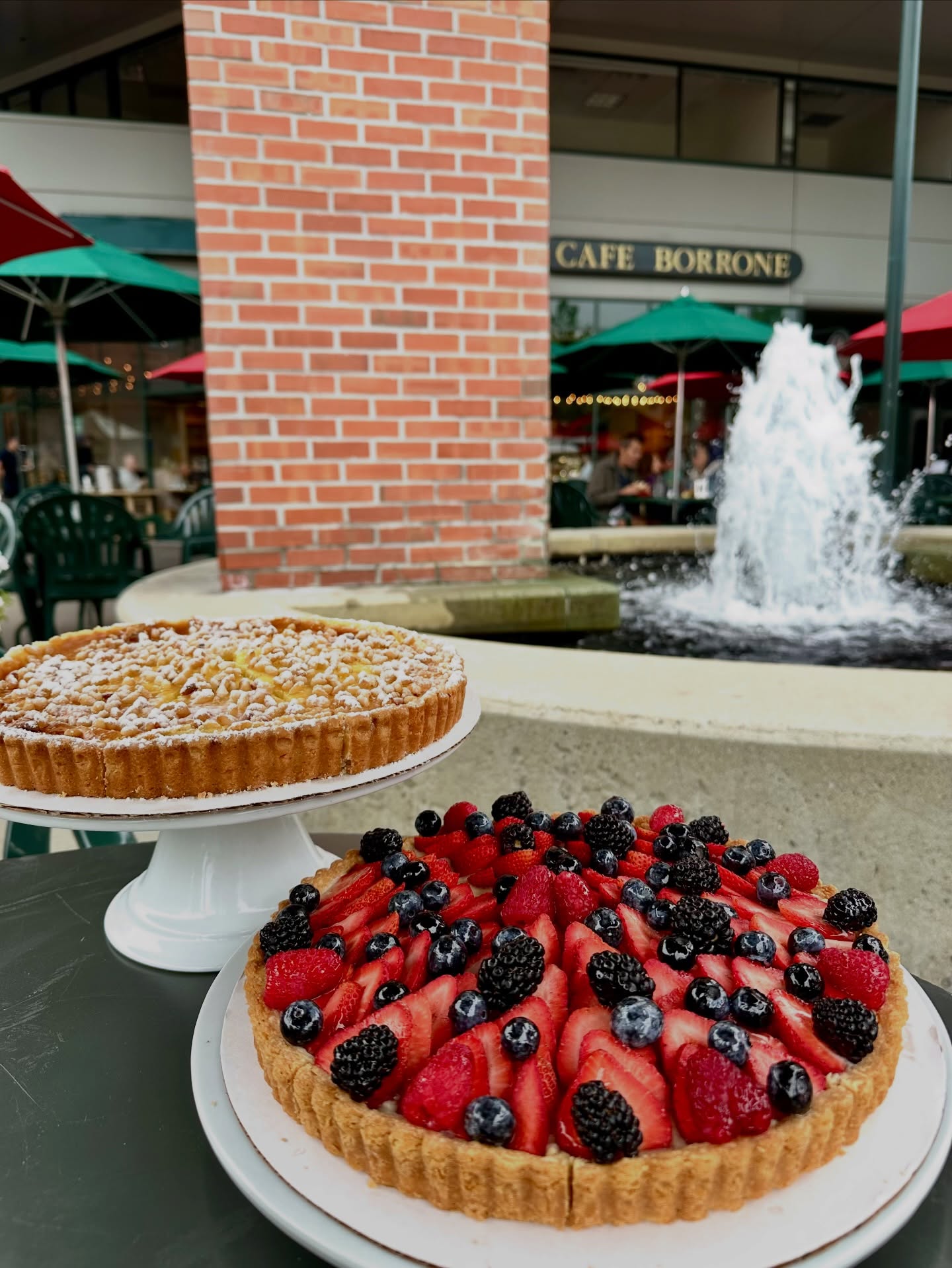 Mixed berry tart and nut tart on cake stands by the fountain