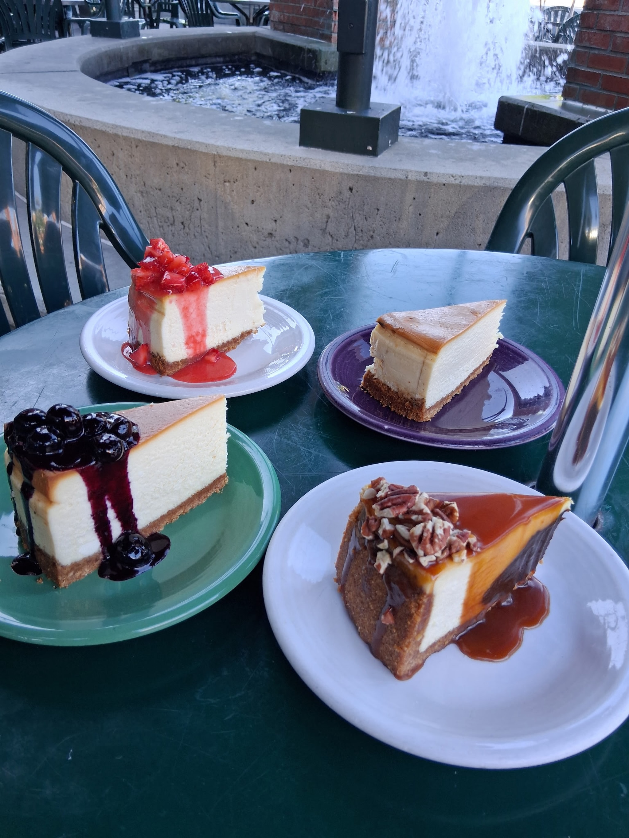 Four slices of cheesecake with strawberry, blueberry, plain and caramel pecan toppings by the plaza fountain