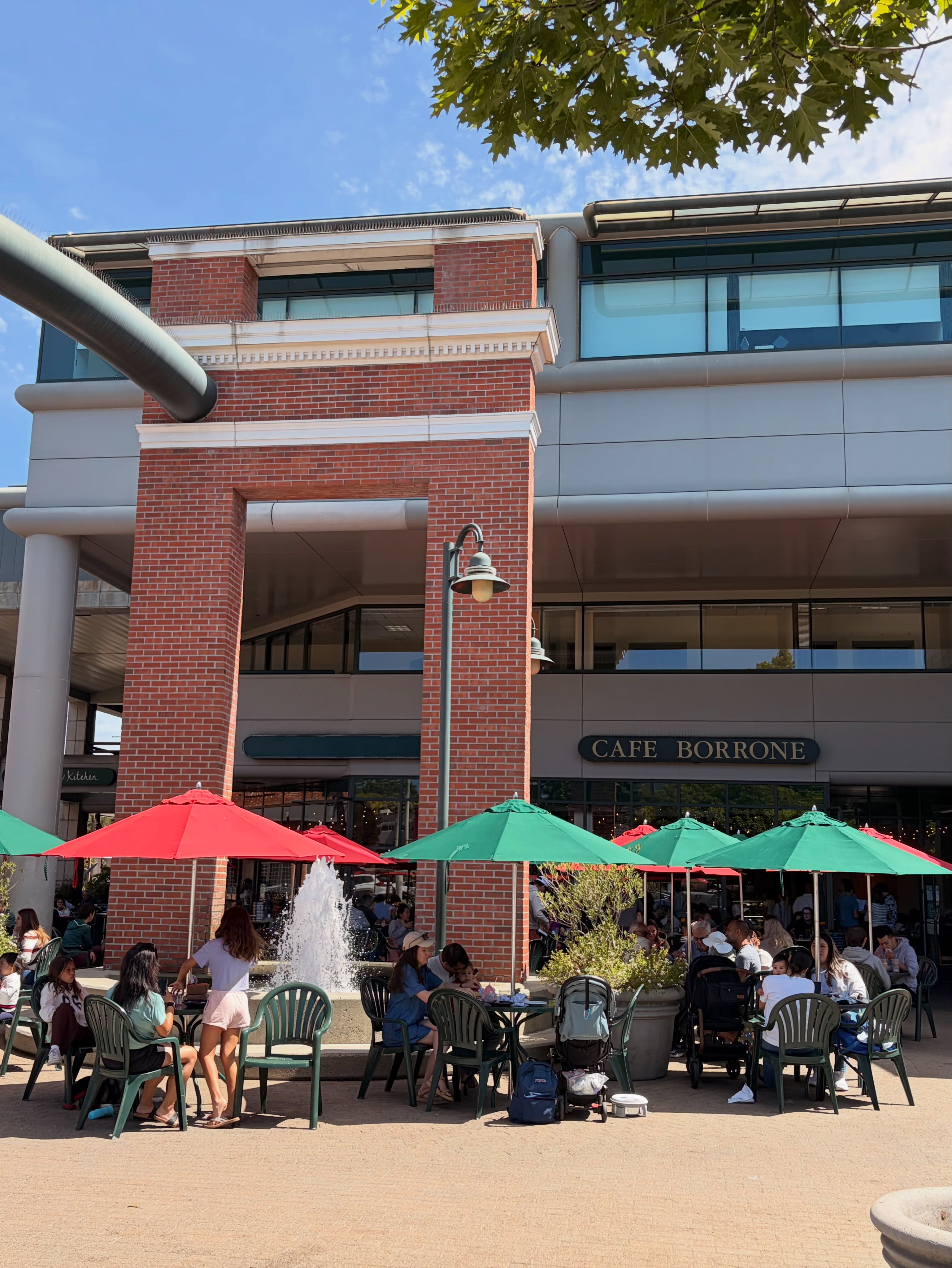 Cafe Borrone storefront with red and green umbrellas on the sunny plaza patio