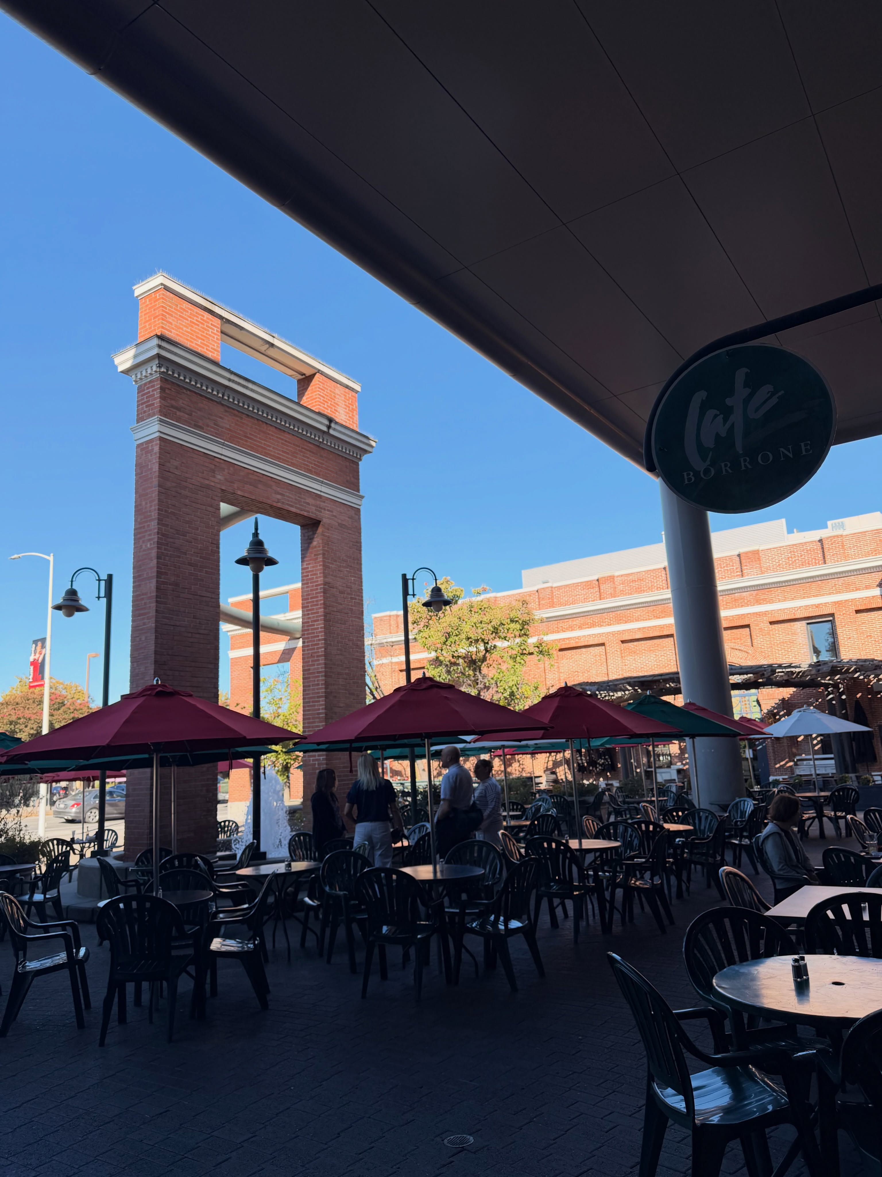 Patio seating under maroon umbrellas beside the brick archway