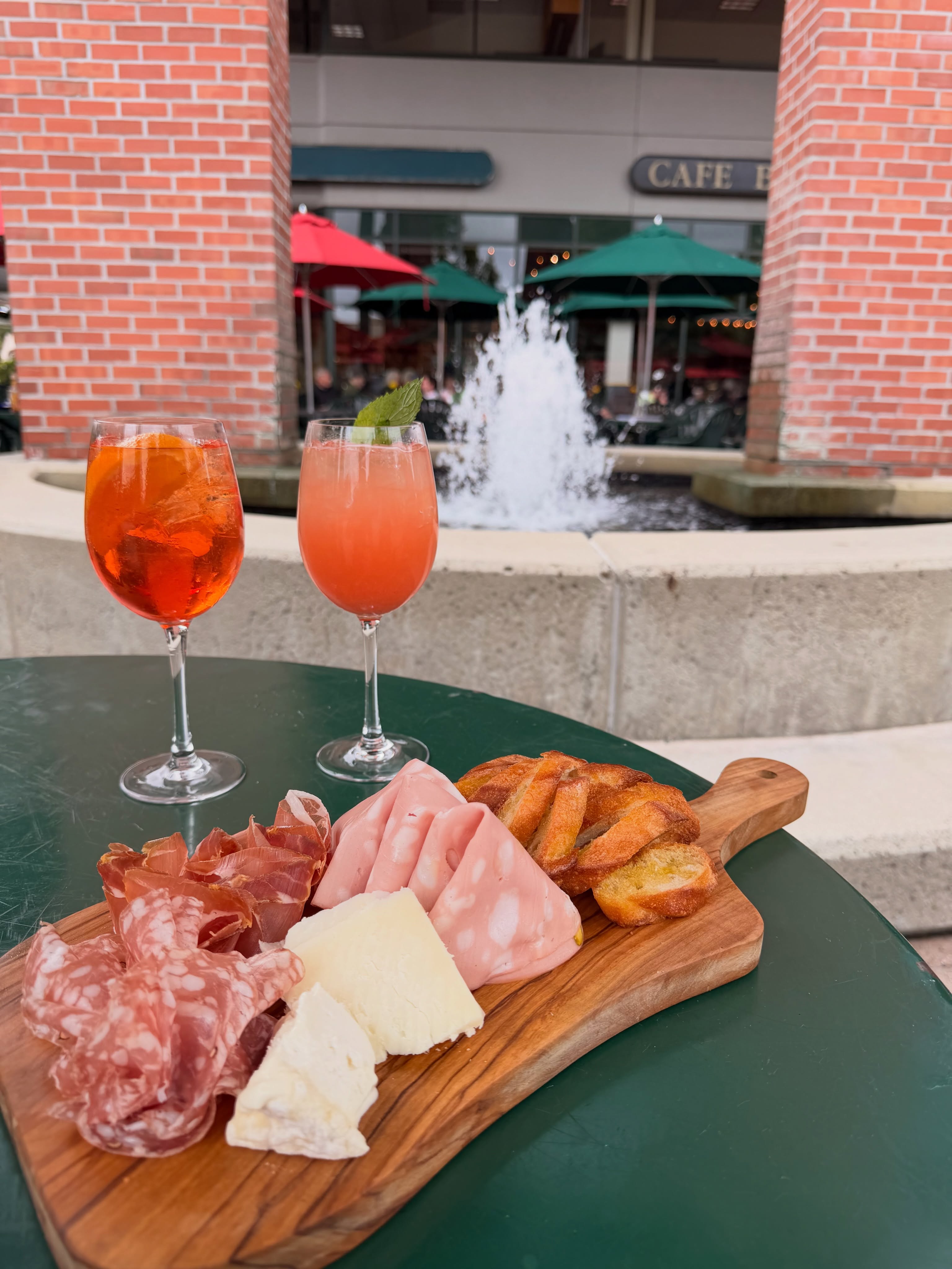 Charcuterie board with cured meats, cheese and bread beside two cocktails